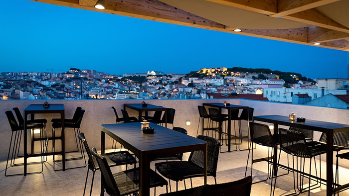 A rooftop terrace at the Lisboa Pessoa Hotel in Lisbon, Portugal. The city at dusk can be seen in the background.