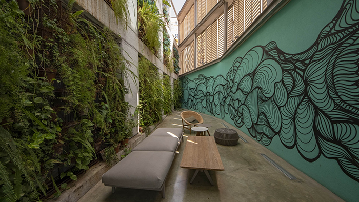 Outdoor seating at the Hotel REC in Barcelona, Spain. The left wall is covered in plants, while the right wall is decorated with a mural.