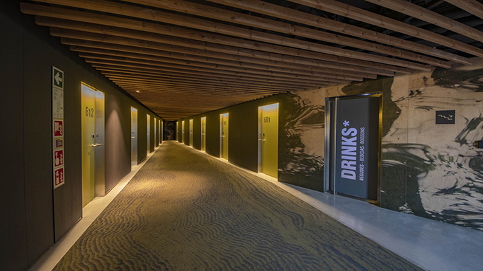 A long hallway inside the Hotel REC in Barcelona, Spain. Both sides of the walkway are lined with greenish yellow doors that each have room numbers printed on them.