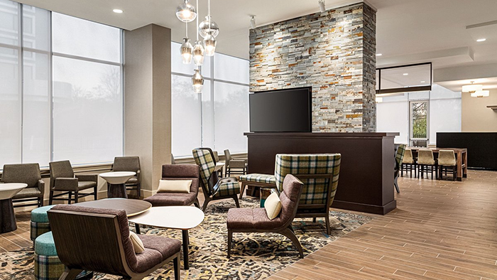 A common area for guests inside the Residence Inn by Marriott New York JFK Airport. There's an interestingly patterned carpet lying underneath several chairs.