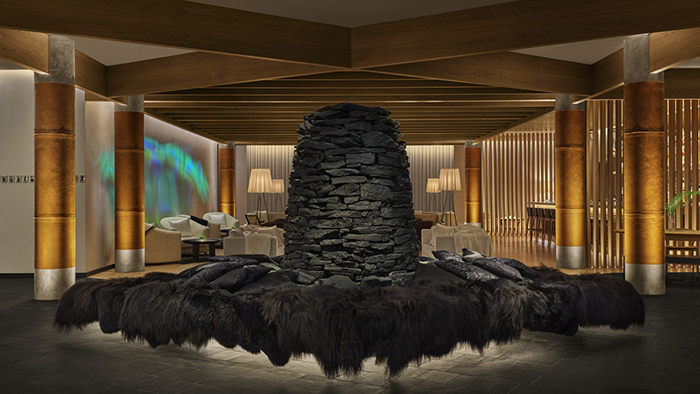 The main lobby inside The Reykjavik EDITION. A neat pile of black stones in the center of the room is surrounded by an incredibly comfortable-looking lounge structure.
