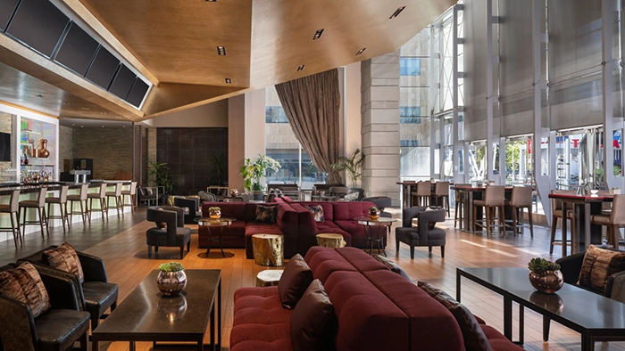 A common area inside The Ritz-Carlton, Los Angeles. There's a bar on the left side of the image and several large windows on the right.