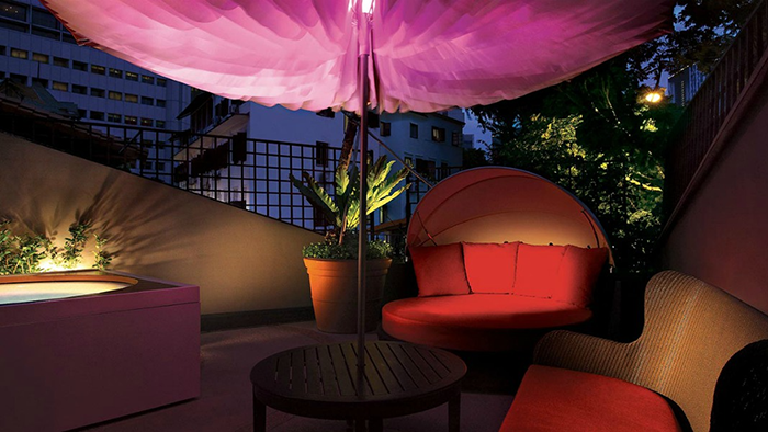 A balcony attached to one of the guest rooms at the Scarlet Singapore. A pink light illuminates the underside of an umbrella.