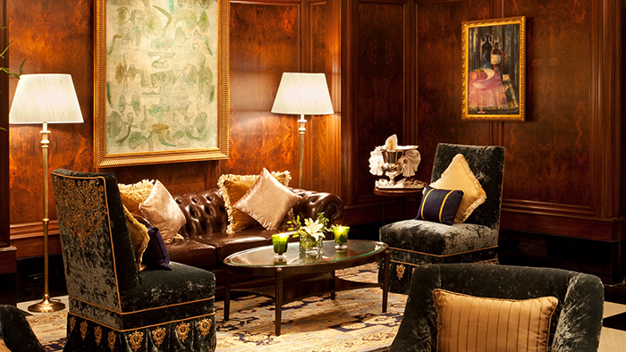 A lounge area in The Taj Mahal Palace Hotel. It looks quite elegant, with opulent furniture and a couple paintings hanging from the dark wood walls.
