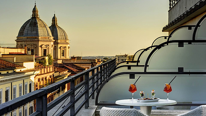 The view from a guest balcony at UNAHOTELS Dec Roma. A couple drinks and a little snack sit on a table in the foreground of the image.