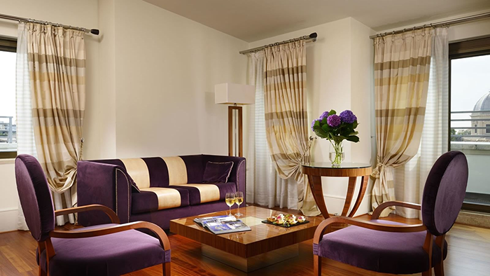 The interior of one of the guest suites at UNAHOTELS Dec Roma. The purple furniture matches an arrangement of flowers.