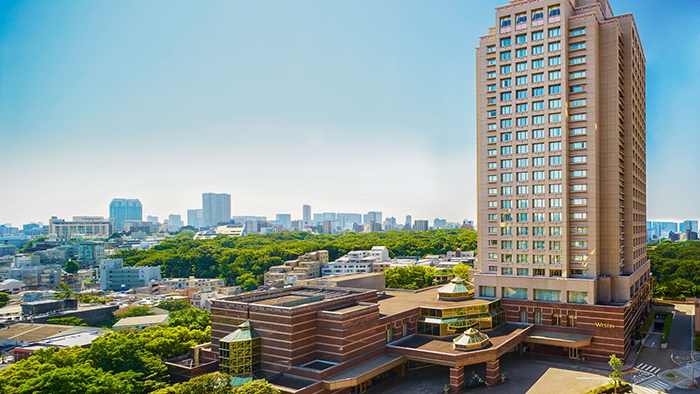 The exterior of The Westin Tokyo. The Tokyo skyline is visible in the background, just beyond a tree-filled park.