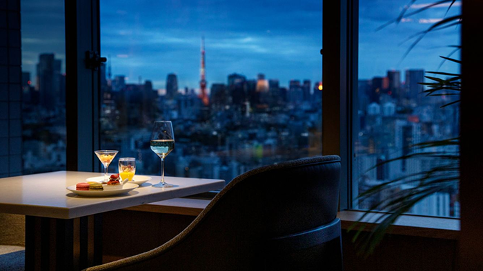 A light snack featuring white wine and macarons inside The Westin Tokyo. Tokyo at dusk is visible in the background.